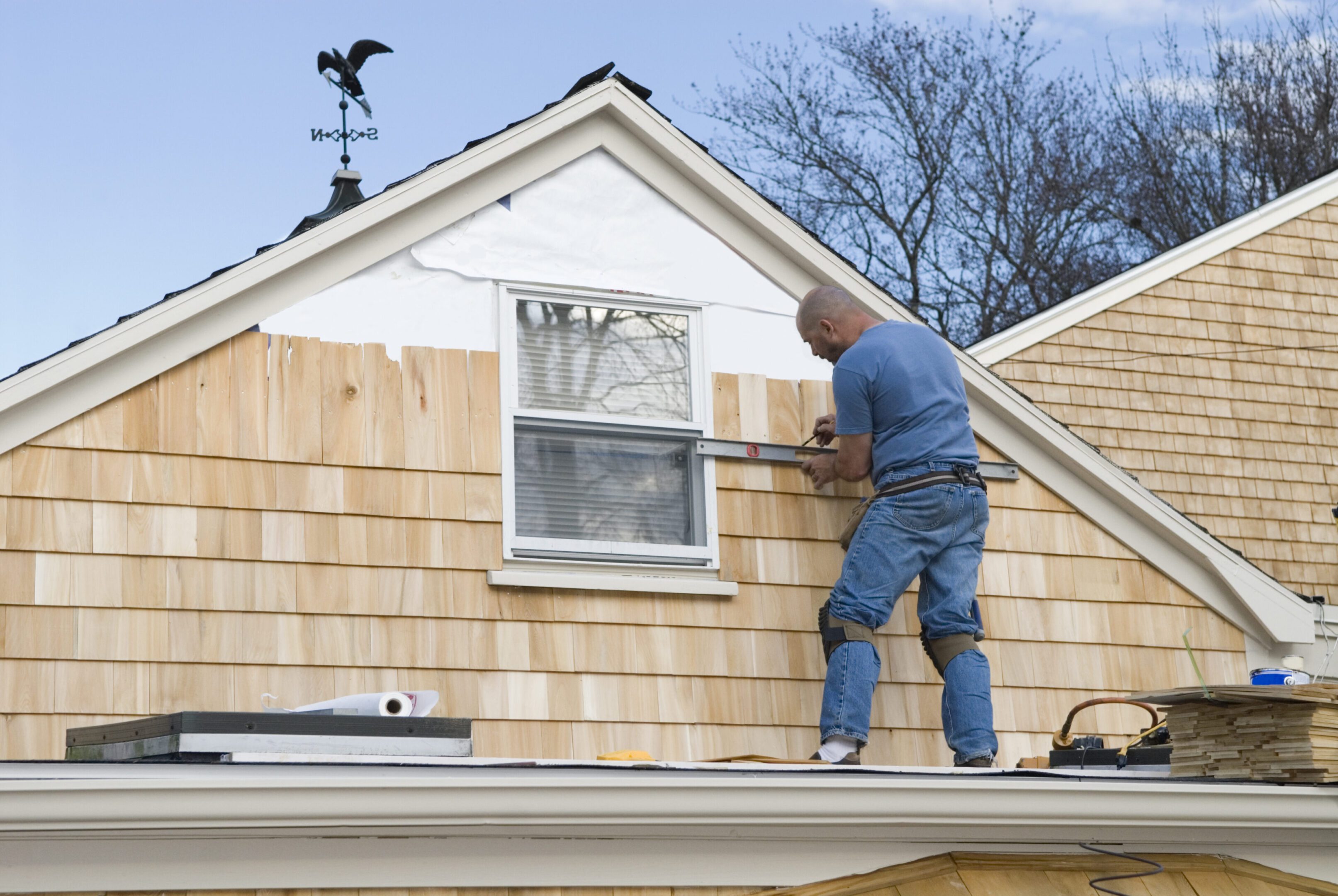 Man painting house exterior on ladder.