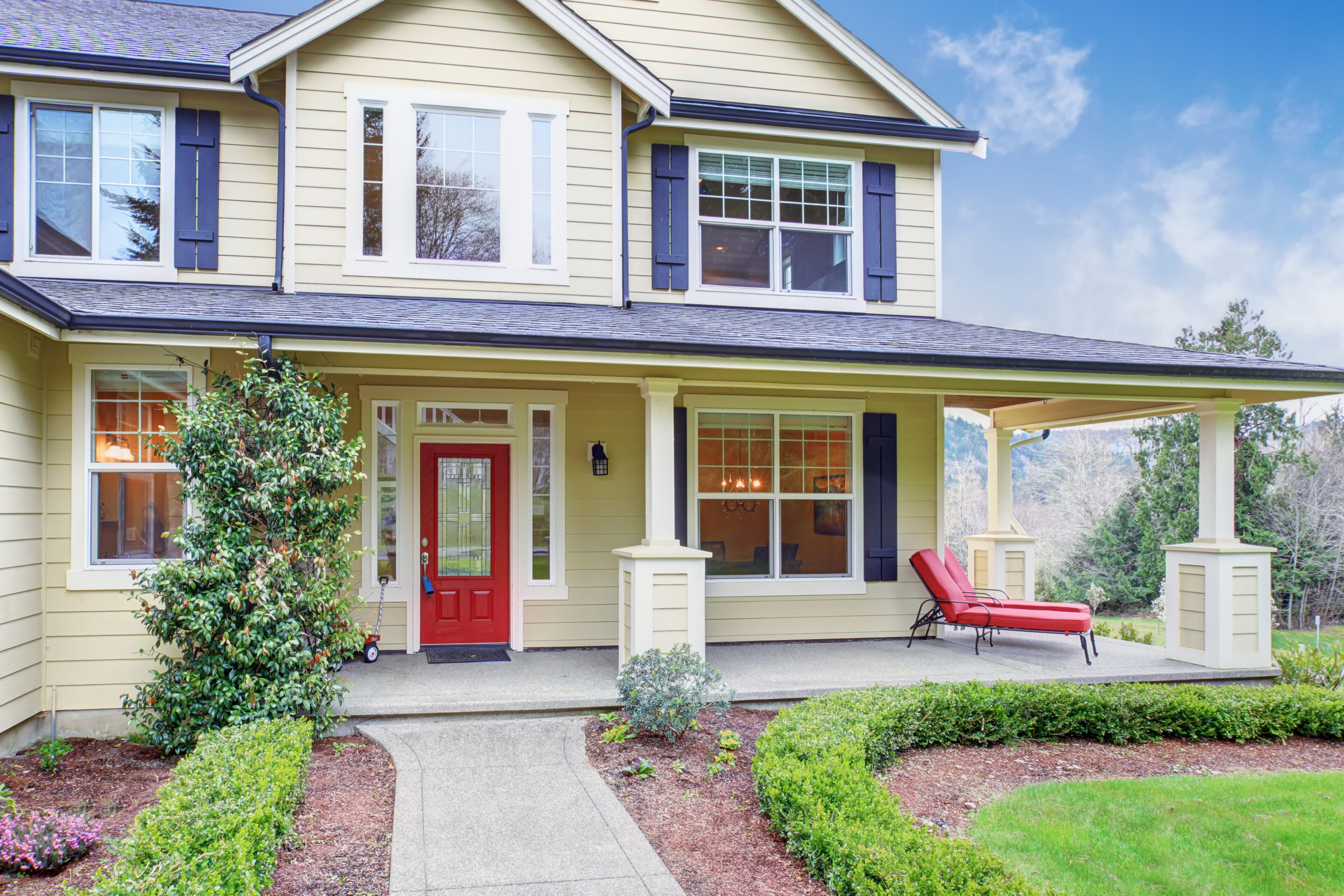 Yellow house with porch and red door.